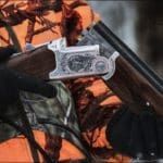 Hunter Hunting in winter with over-under shotgun wearing blaze orange hunting clothing