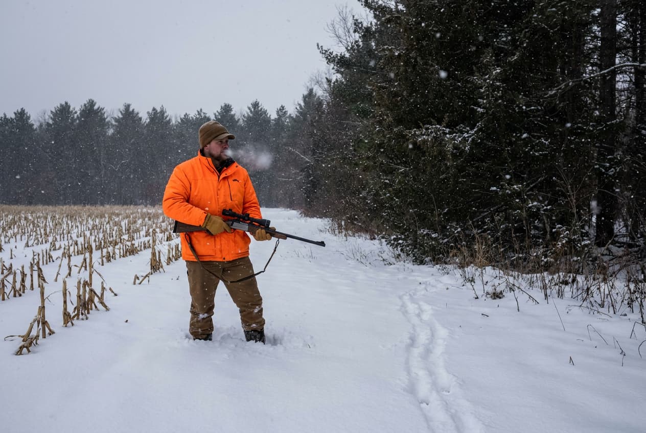 Hunter with a muzzleloader at a snowy Minnesota cornfield edge during late deer season Hunter with a muzzleloader at a snowy Minnesota cornfield edge during late deer season